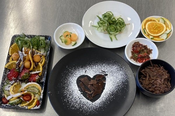 Three plates and four bowls showing food prepared in the high school kitchen.